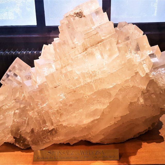 Un grand bloc de sel de Wieliczka, exposé au Musée d'Histoire Naturelle de Vienne. Le bloc de sel a une structure cristalline et repose sur une base en bois avec une inscription.
