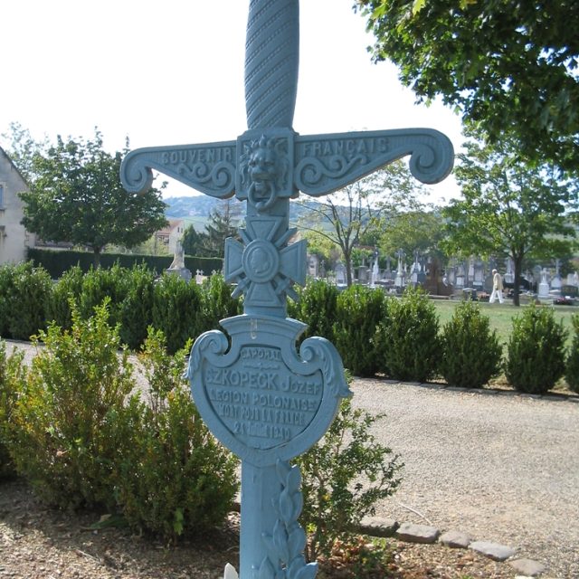 Tombe d'un soldat de la 10e brigade de cavalerie blindée dans le carré des combattants d'un cimetière municipal. La tombe comporte une croix avec des inscriptions et des éléments décoratifs, entourée de verdure.
