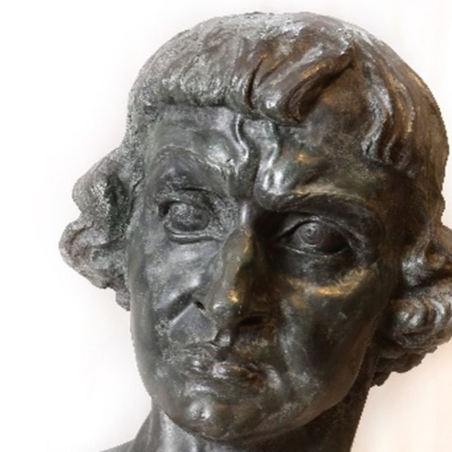 Une sculpture en bronze représentant la tête d'un homme aux cheveux bouclés et à l'expression sérieuse, intitulée « Autoportrait en Copernic » et réalisée par Stanisław Szukalski.