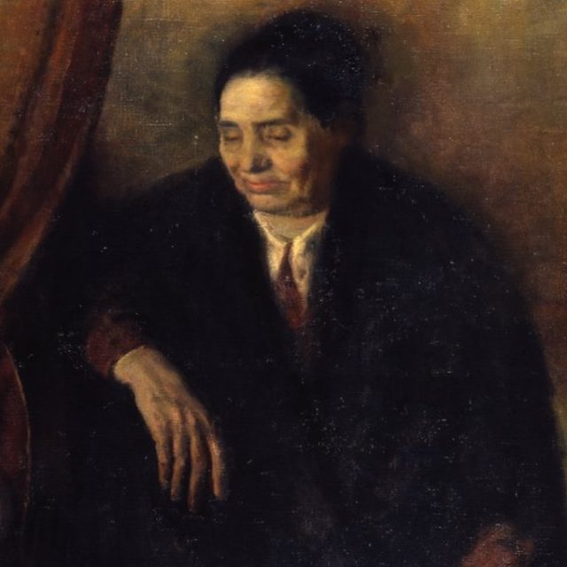 Image d'une femme âgée aux yeux fermés, vêtue d'un châle sombre, assise sur un fond marron.