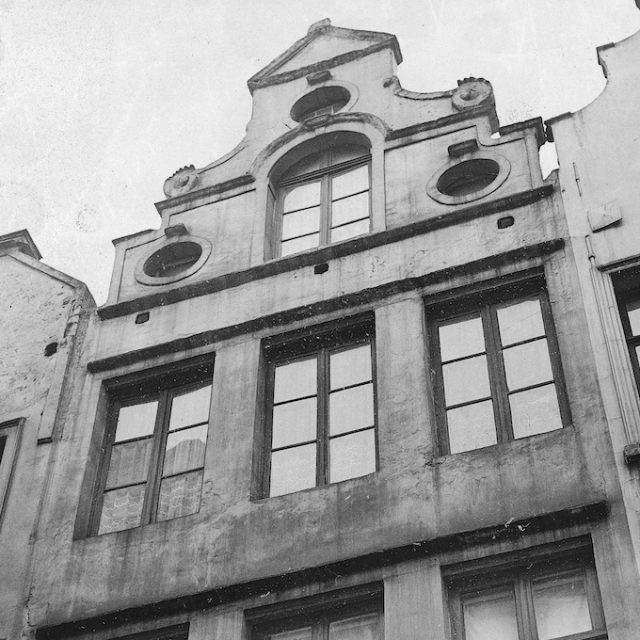 Black and white photo of a townhouse facade in Brussels with tall windows and a decorative gable with oval openings
