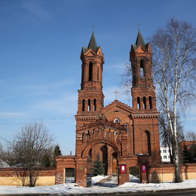 Photograph of Saint Barbara Church in Vitebsk, red brick facade with two tall towers and a central gate, snow on the ground and leafless trees