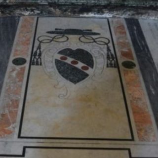 Marble floor tomb slab in the Il Gesu church in Rome with a large coat of arms under a bishops hat with tassels and a red and black border