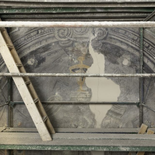 Photo d un echafaudage et d une echelle contre un mur d eglise avec une peinture murale partiellement degagee montrant une arche et un motif de croix doree, Drohobych