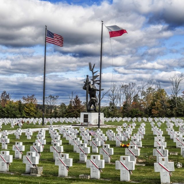 Monument in Doylestown among rows of white crosses with Polish and American flags on tall poles.
