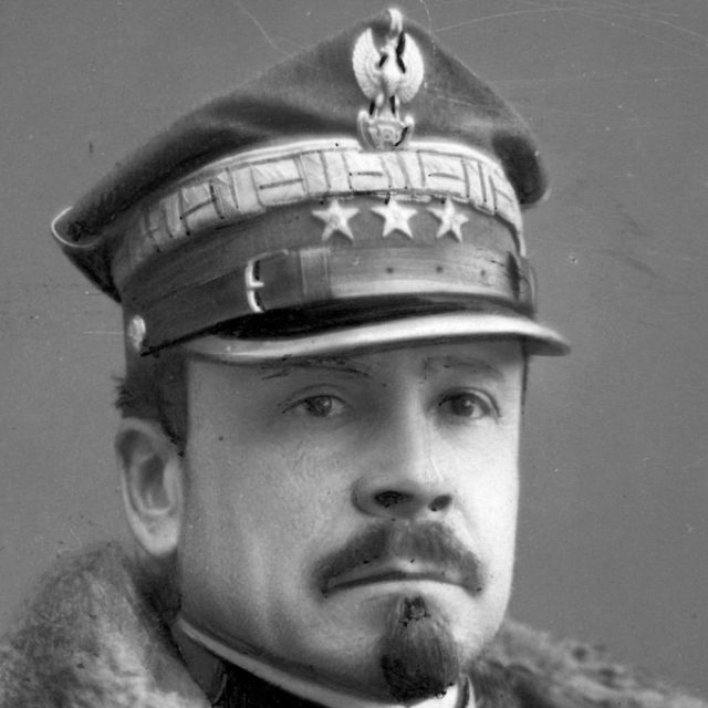 Black and white portrait of a man with a mustache and pointed beard in a military cap with an eagle emblem and three stars.
