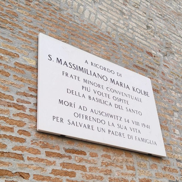 Tablica pamiątkowa na ceglanej ścianie w Padwie z włoskim napisem wymieniającym Massimiliano Maria Kolbe i Auschwitz 14 VIII 1941.