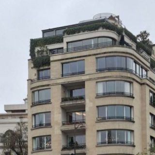 Photographie des étages supérieurs de l'immeuble des Cierplikowski à Paris, avec sa façade semi-circulaire, ses grandes fenêtres, ses balcons et ses terrasses agrémentées de plantes sur le toit.