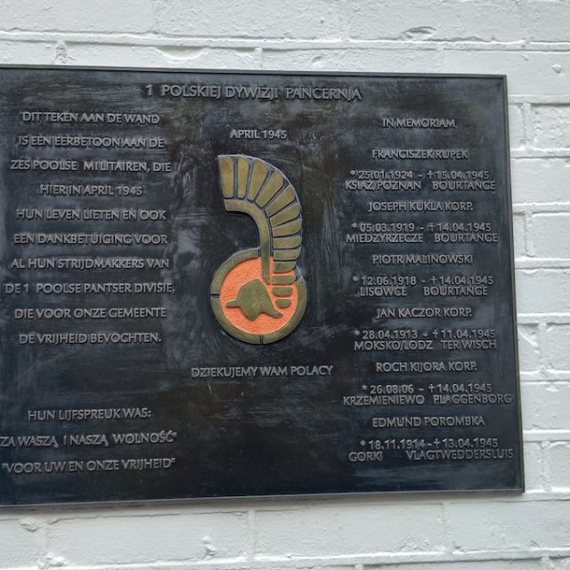 Plaque commémorative de la 1re division blindée polonaise sur un mur de briques blanches à Bourtange avec des inscriptions en polonais et en néerlandais et un emblème au centre.