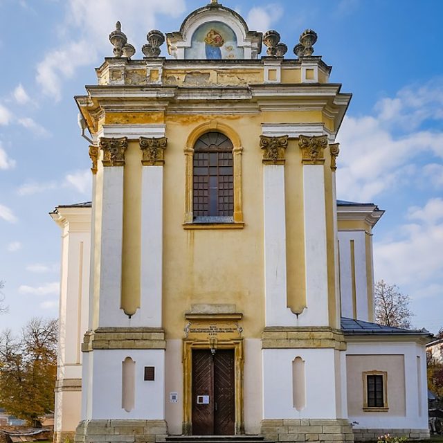 Front facade of the Parish Church of the Assumption in Buchach with pilasters, a tall central window, a painted panel above the cornice and a dark entrance door.